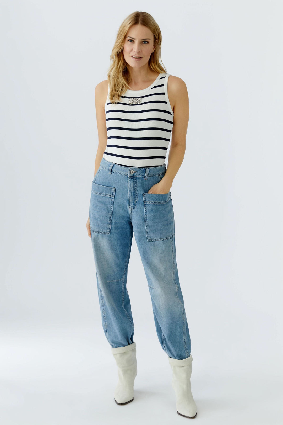 Femme portant une camisole rayée sans manches avec jeans et bottes blanches, style marin élégant et silhouette féminine.