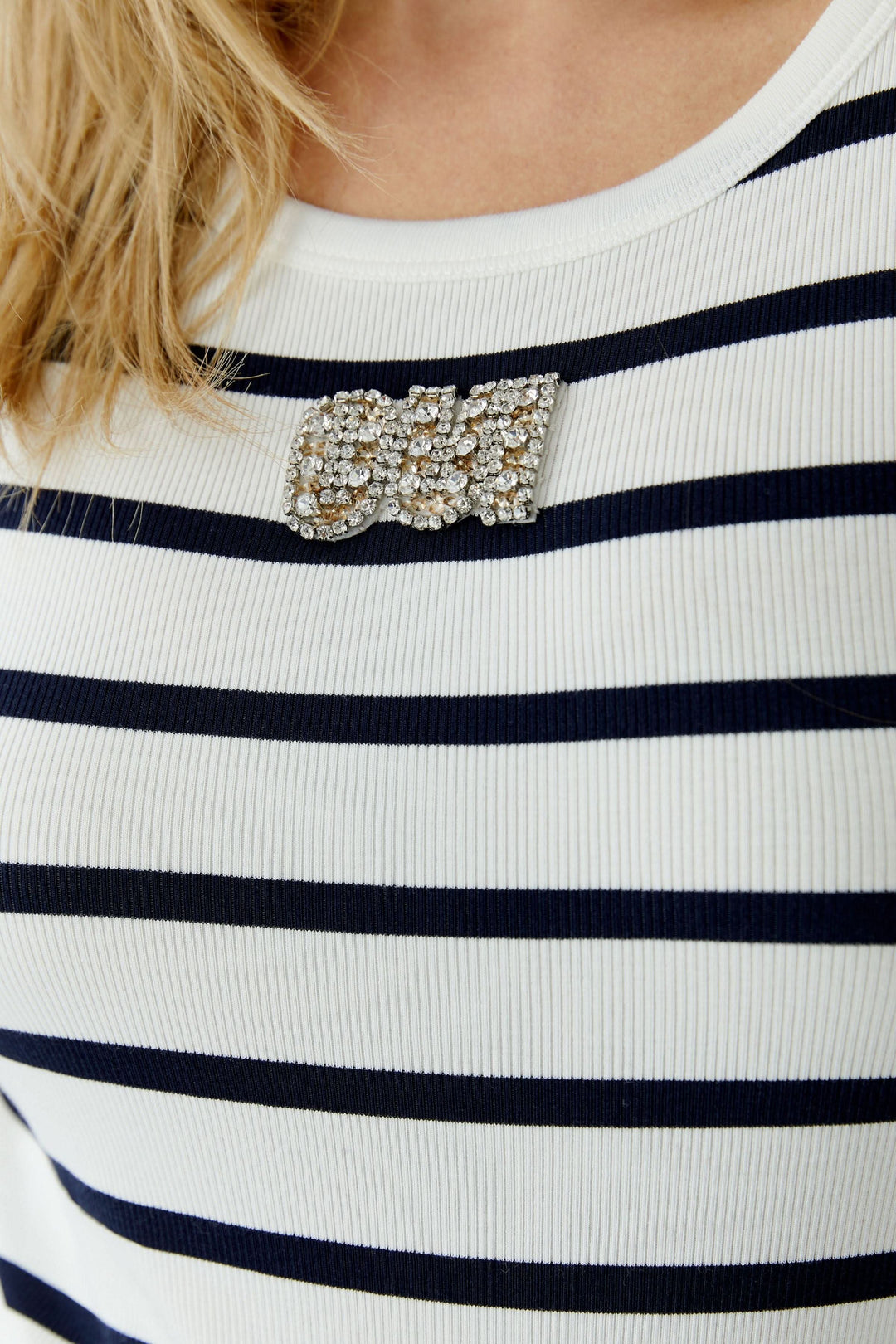 Camisole rayée sans manches avec motif horizontal, affichant un style marin revisité et épuré, ornée d'une broche élégante.