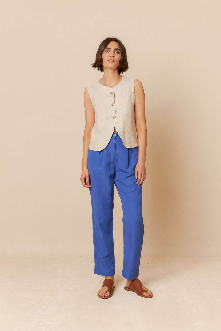 Camisole sans manches en lin avec boutons, portée avec un pantalon bleu, look décontracté.