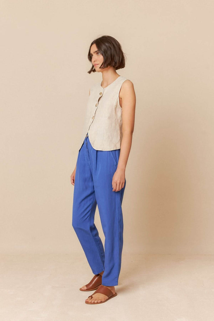 Camisole sans manches en lin avec boutons, portée avec un pantalon bleu et des sandales, pour un look décontracté.