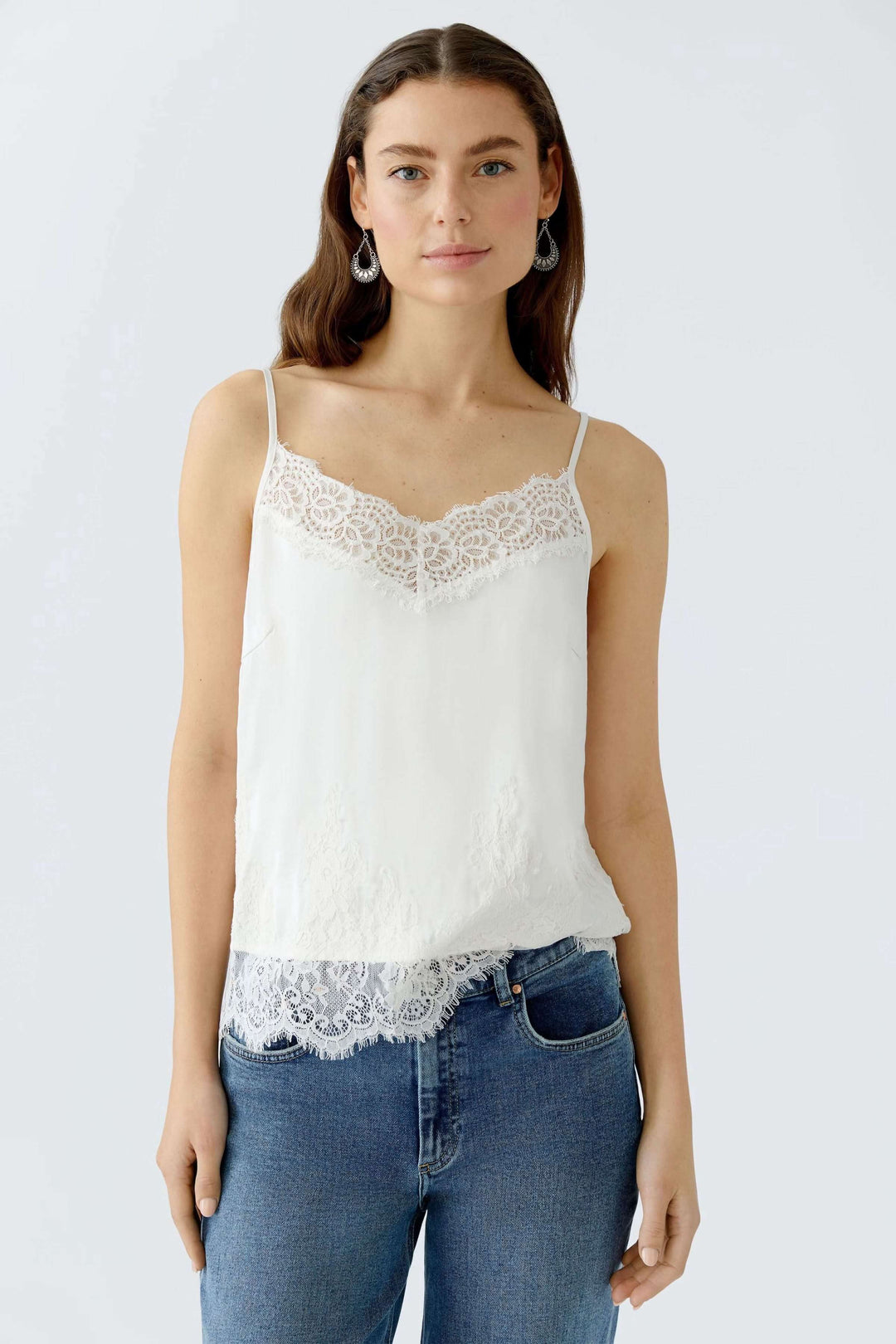 Camisole satinée avec dentelle blanche, décolleté en V et bretelles spaghetti, portée avec un jean.
