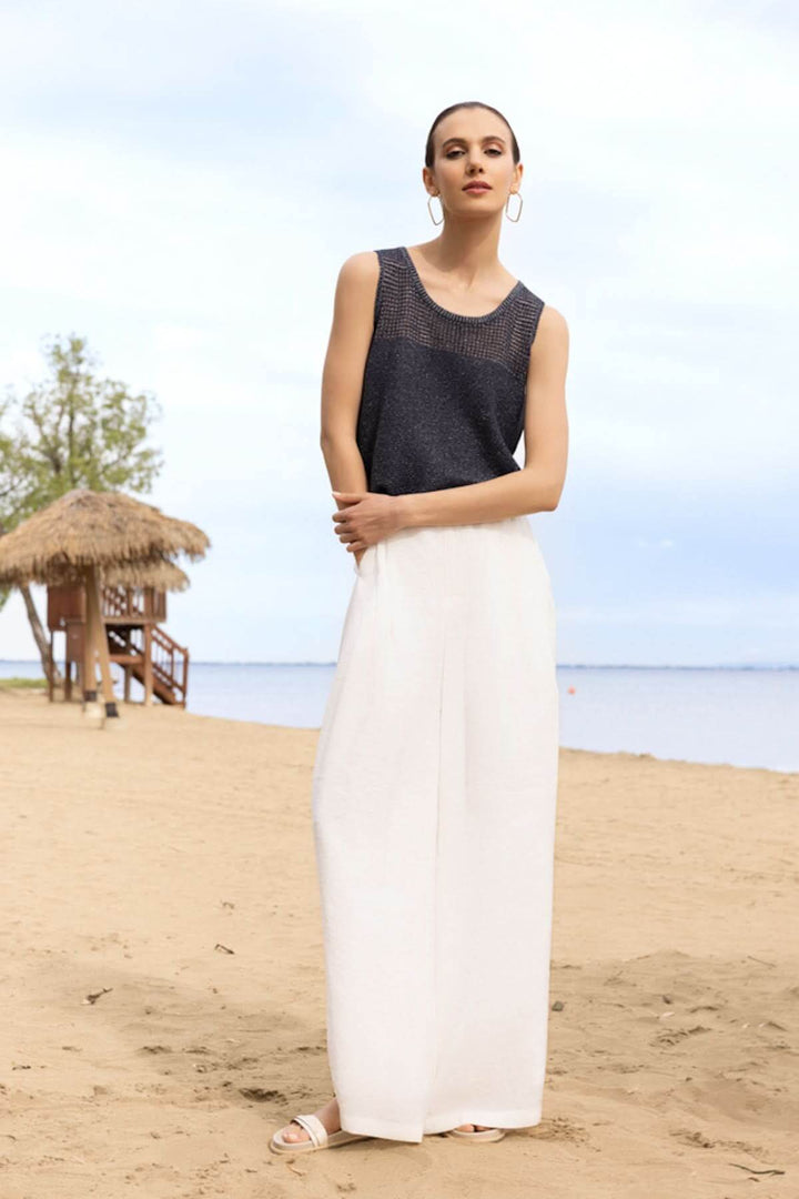 Femme portant une camisole texturée ajourée sur une plage, idéale pour un look moderne et léger.