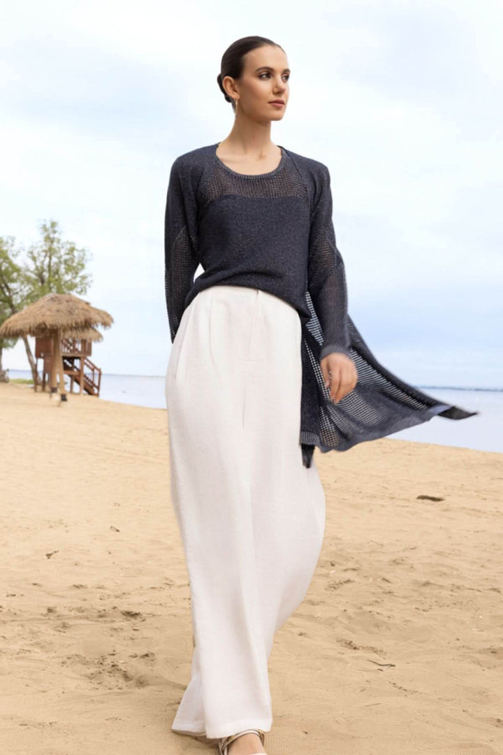 Femme sur la plage portant une camisole texturée ajourée avec une jupe blanche, toile de fond mer et ciel.