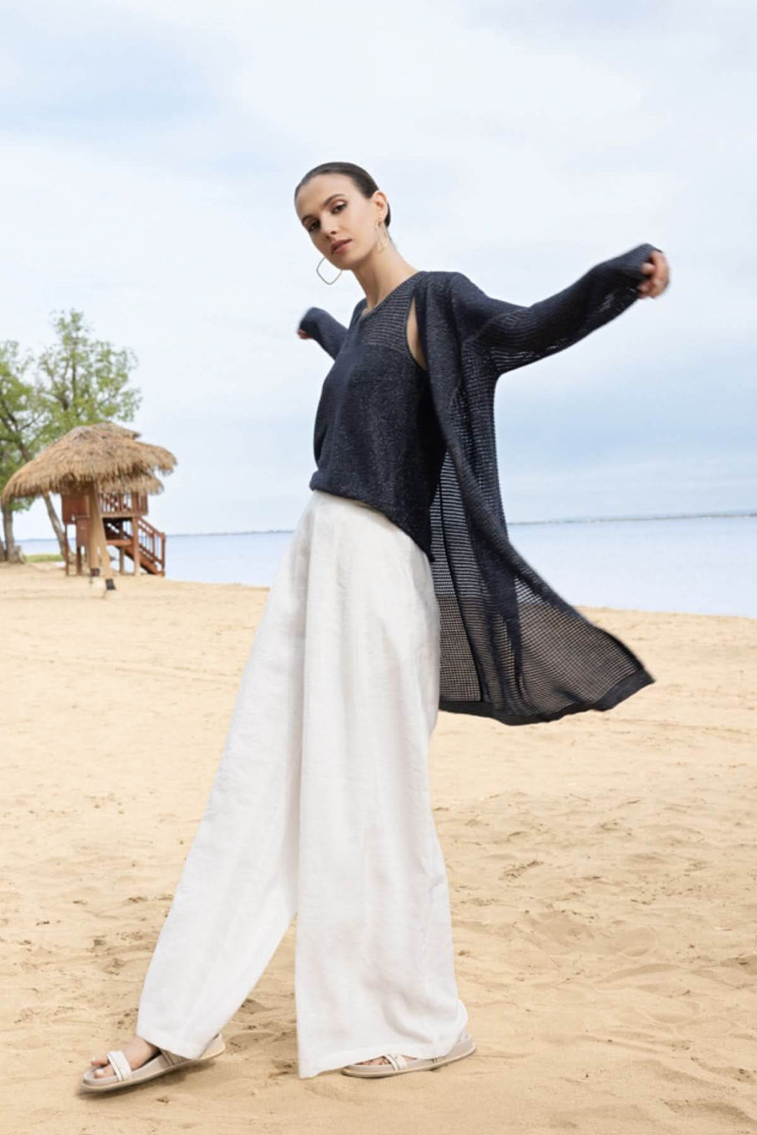 Femme portant une camisole texturée ajourée sur une plage, ajoutant une touche moderne et légère à une tenue estivale élégante.