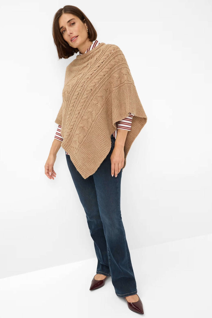 Femme portant la Cape Thea en tricot torsadé asymétrique beige, tenue élégante pour mi-saison, décris moi le produit en français.