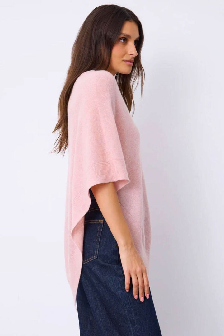 Femme portant une cape en maille rose asymétrique pour une silhouette fluide et élégante, parfaite pour la superposition.