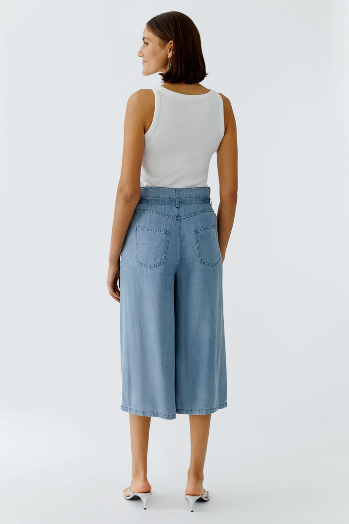Femme portant un capri denim à jambe large et un haut blanc, vue de dos. Mode décontractée et moderne.