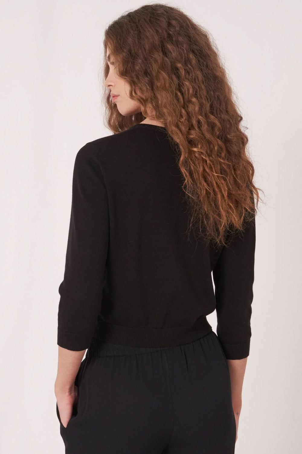 Femme vue de dos portant un cardigan court noir avec des manches longues et une coupe près du corps.