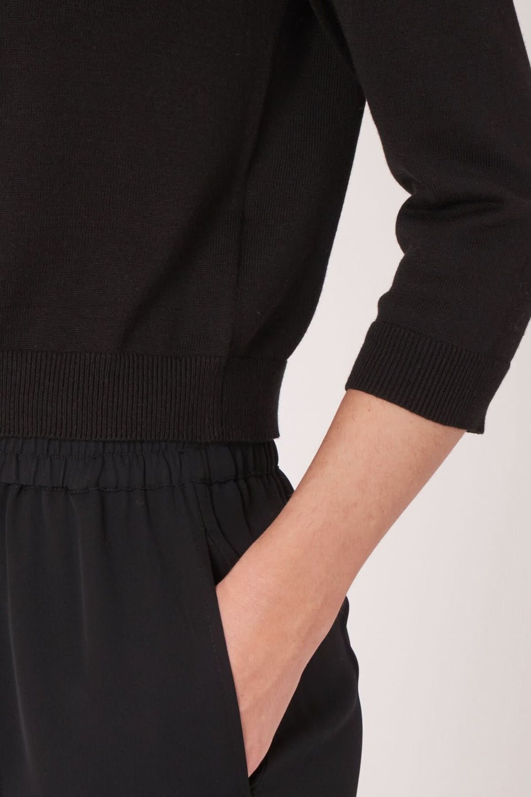 Détail d'un cardigan noir avec encolure ronde et manches longues, porté avec un pantalon noir.