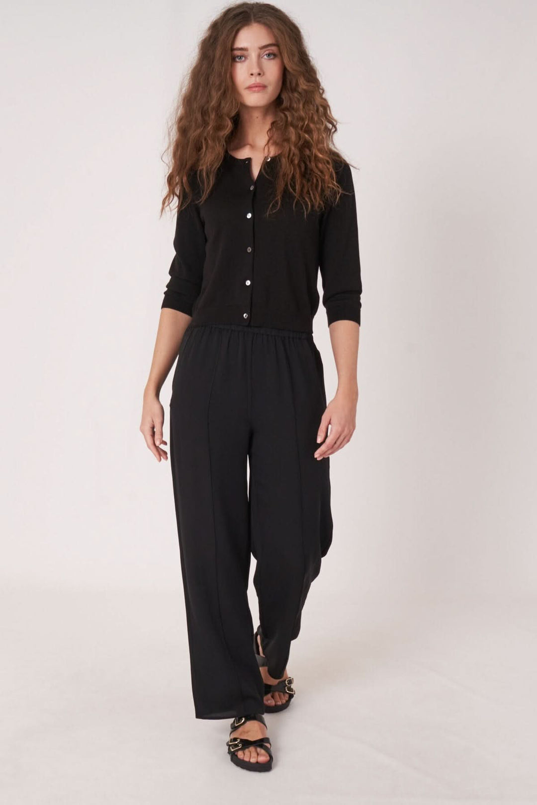 Femme portant un cardigan noir avec des boutons, associé à un pantalon noir fluide, idéale pour un style décontracté.