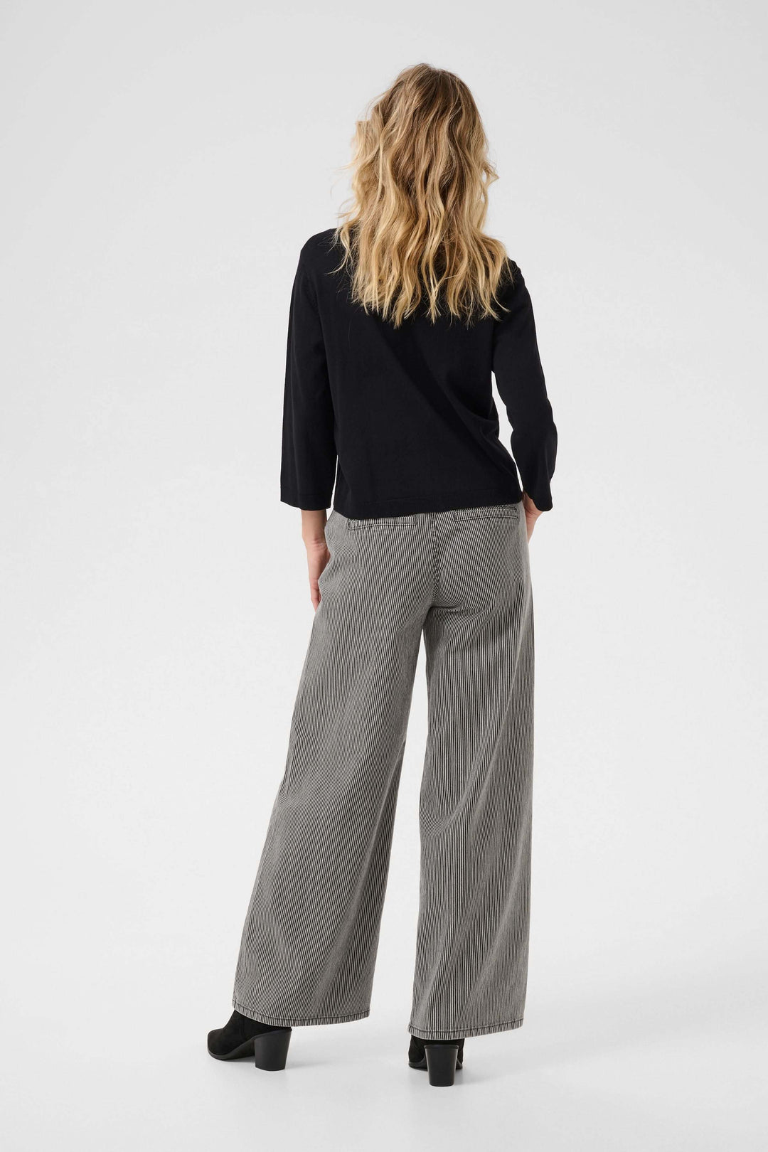 Femme portant une cardigan minimaliste noire à manches trois-quarts et un pantalon large à rayures.