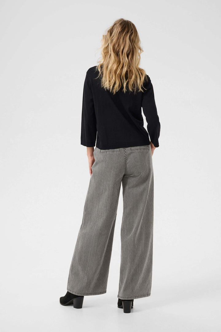 Femme portant une cardigan minimaliste noire à manches trois-quarts et un pantalon large à rayures.