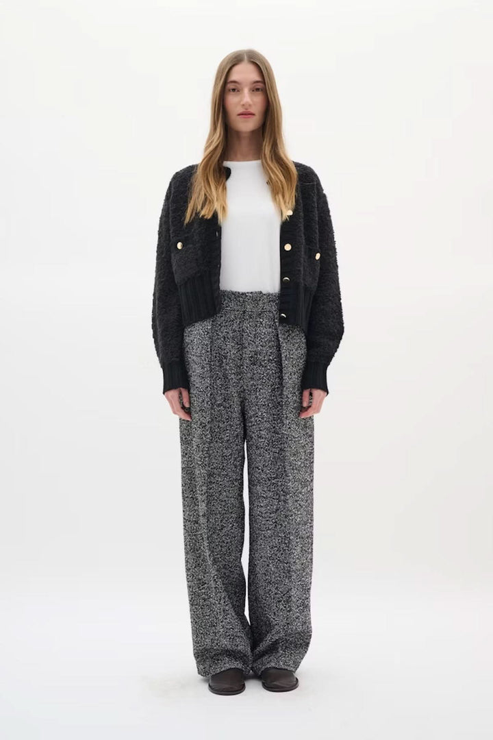 Femme portant le Cardigan Guo noir avec boutons dorés, style moderne, maille texturée, allure chic et sophistiquée, pantalon taille haute.