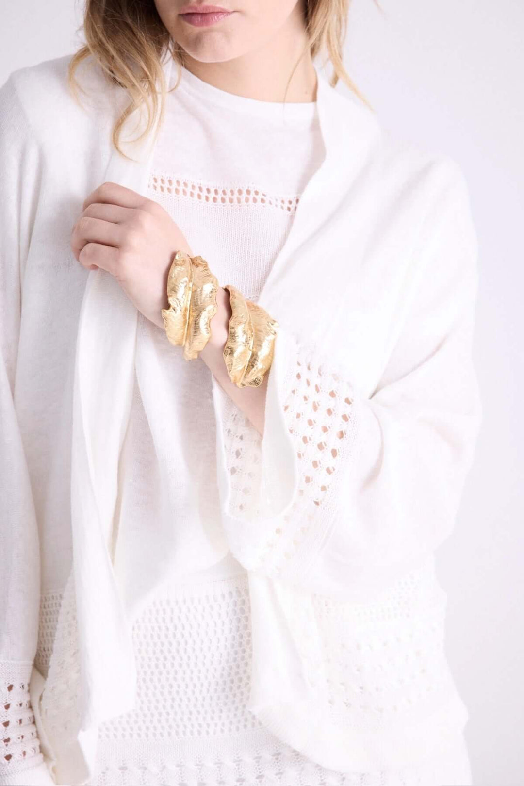 Femme portant un cardigan ouvert blanc avec détails ajourés et un bracelet doré, pour une allure élégante et fluide.