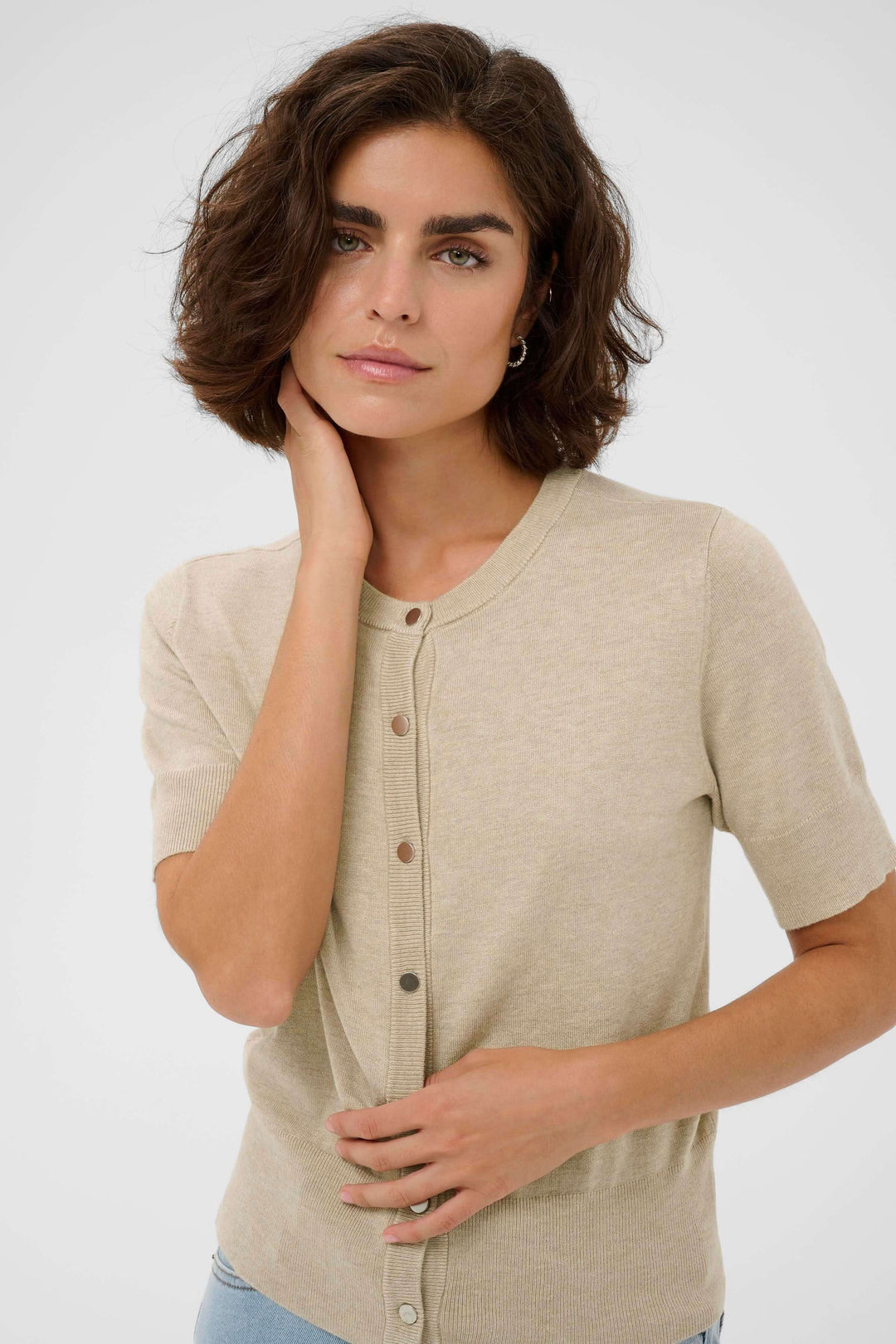 Femme portant le Cardigan Lizza à manches courtes et coupe ajustée, couleur beige, pour un style épuré et polyvalent.