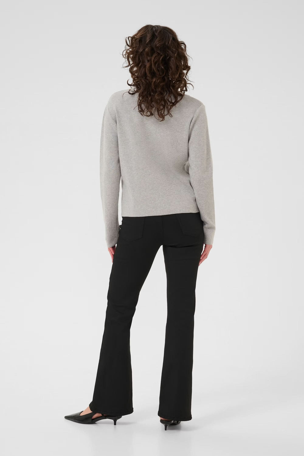 Femme portant un cardigan Visja zippé gris avec col chemise, vu de dos, style minimaliste et moderne, associé à un pantalon noir.
