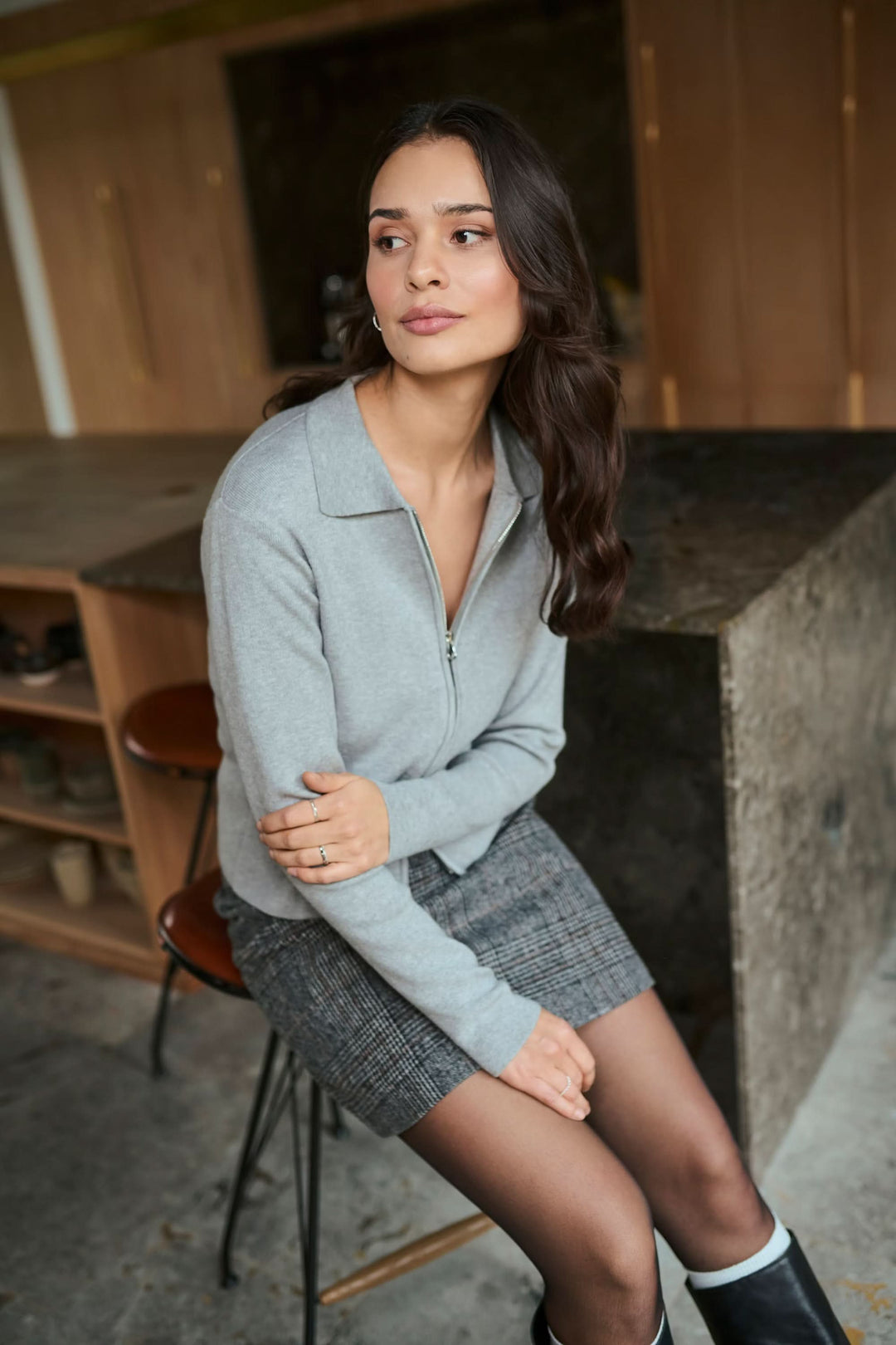 Femme portant un cardigan zippé Visja gris avec col chemise, assise, style minimaliste et moderne, parfait pour un look élégant.