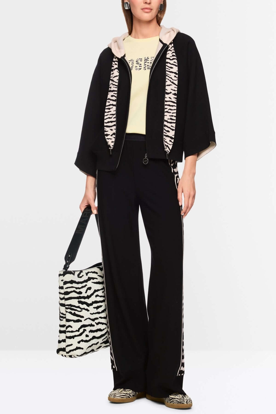 Cardigan avec fermeture éclair moderne, manches larges, capuche avec bande contrastée, ruban imprimé animalier, femme portant un ensemble noir.