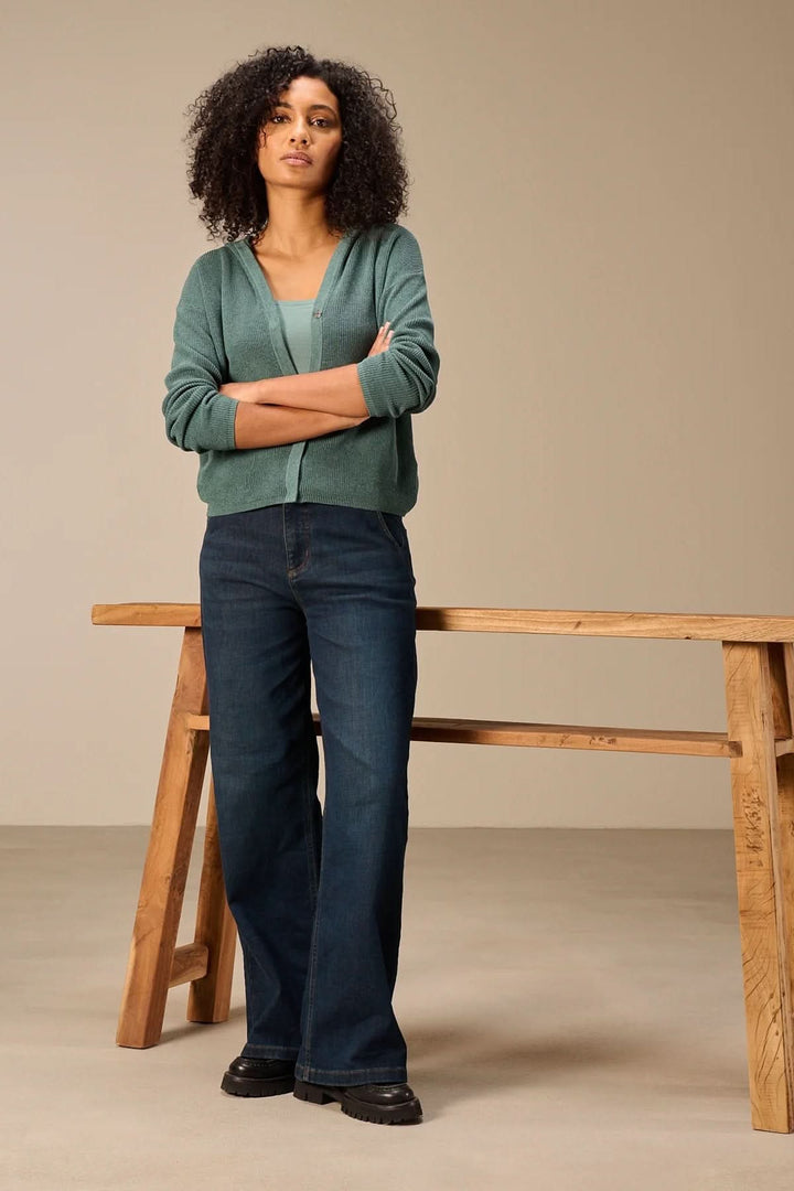 Cardigan à capuche en maille porté par un mannequin posant devant une table en bois, style décontracté et moderne.
