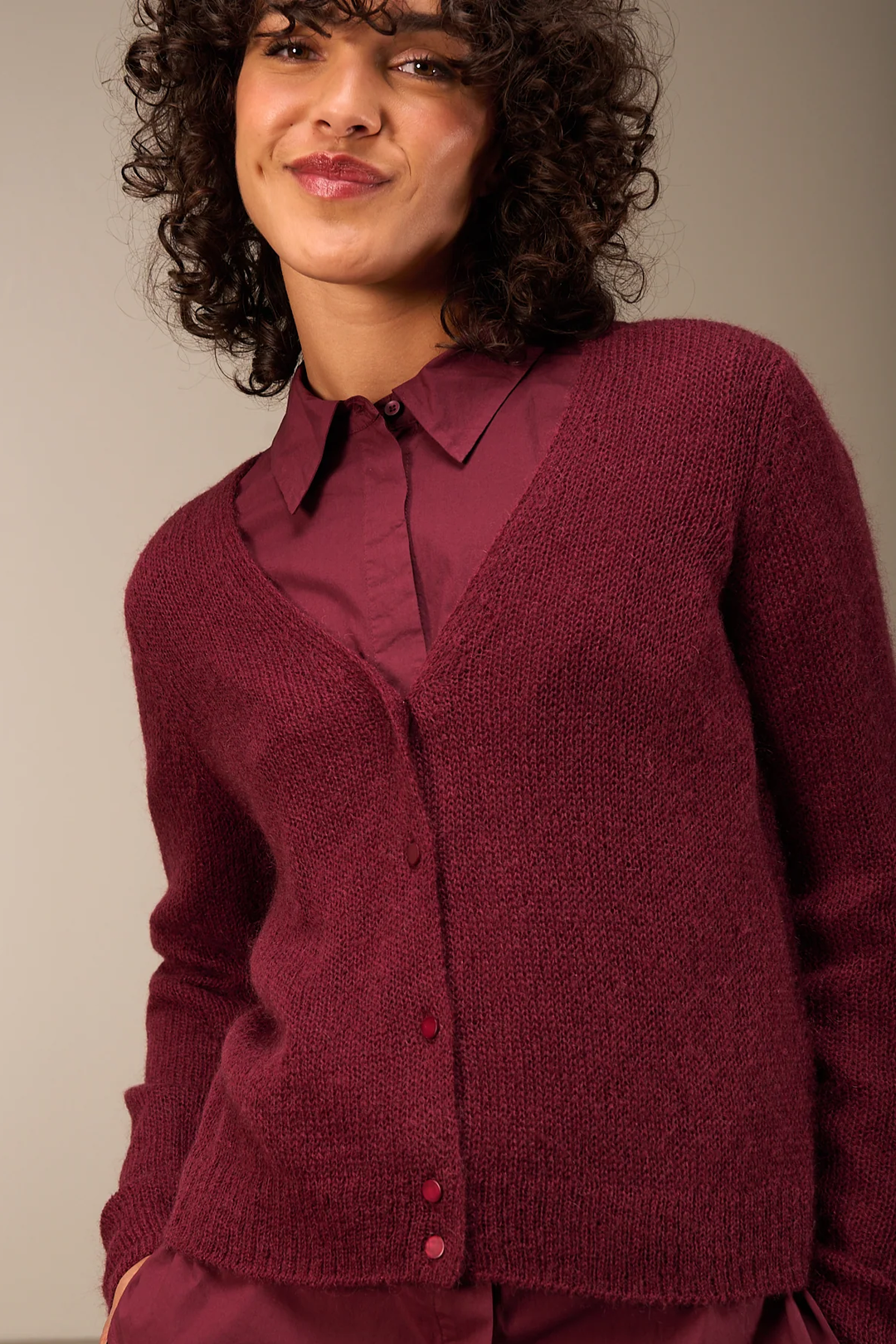 Femme portant un cardigan coupe droite en laine bordeaux avec encolure en V, superposé sur une chemise assortie pour un look élégant.