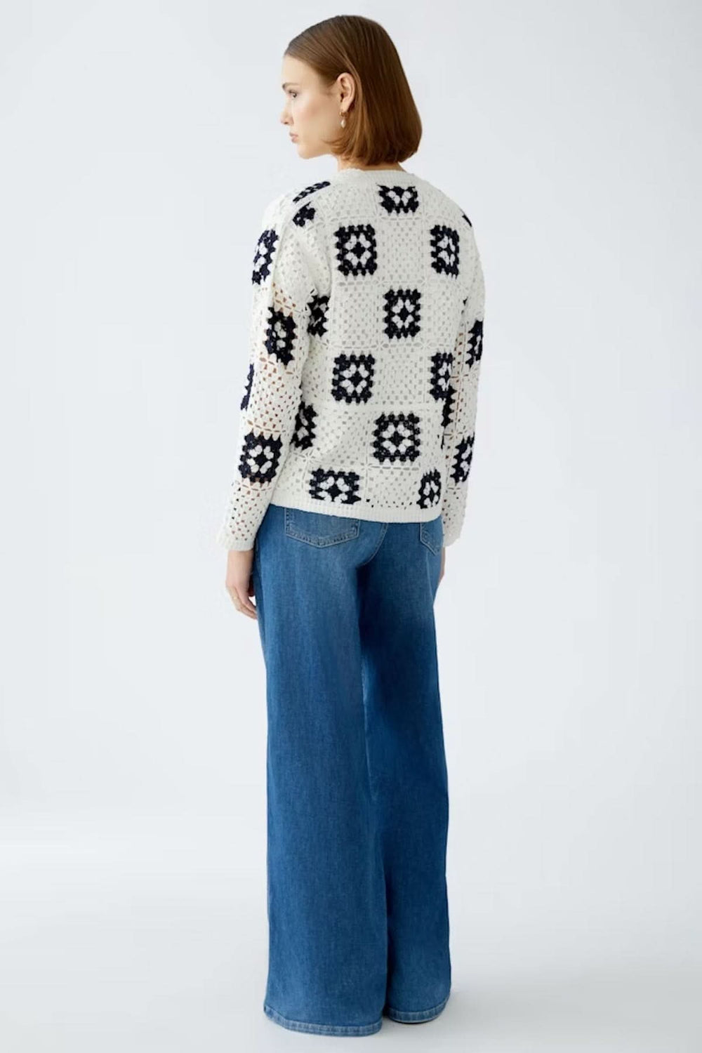 Cardigan en crochet blanc avec motifs géométriques marines, porté avec un jean bleu large.