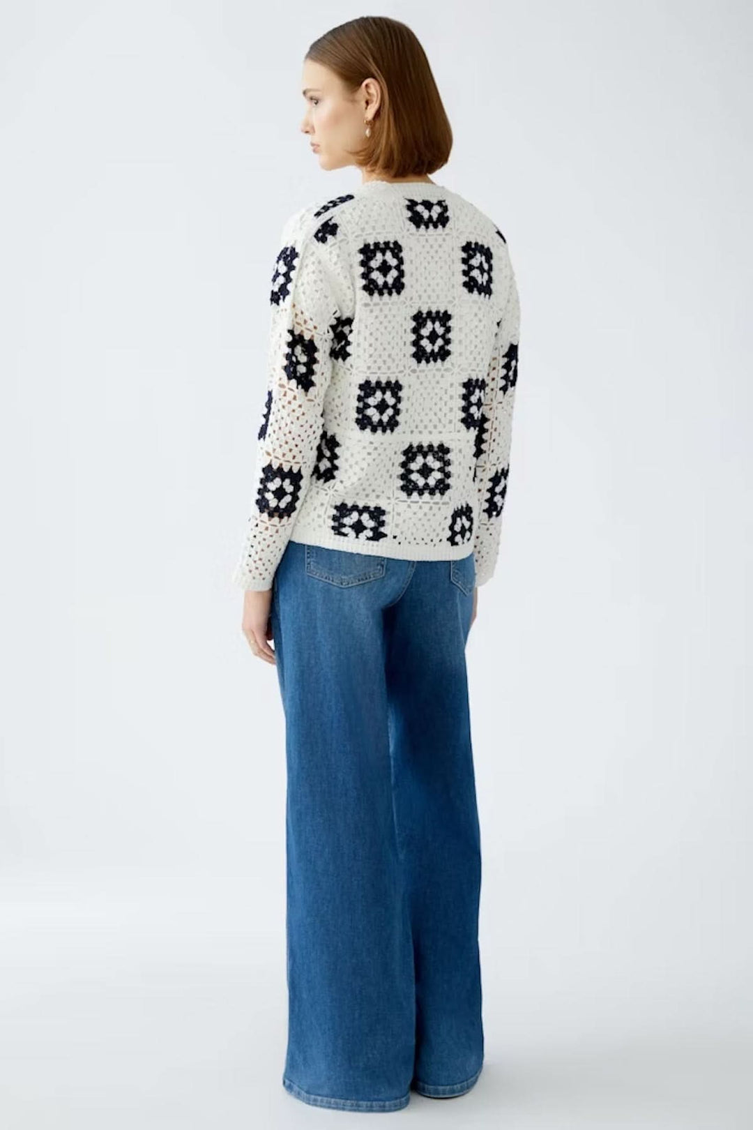 Cardigan en crochet blanc avec motifs géométriques marines, porté avec un jean bleu large.
