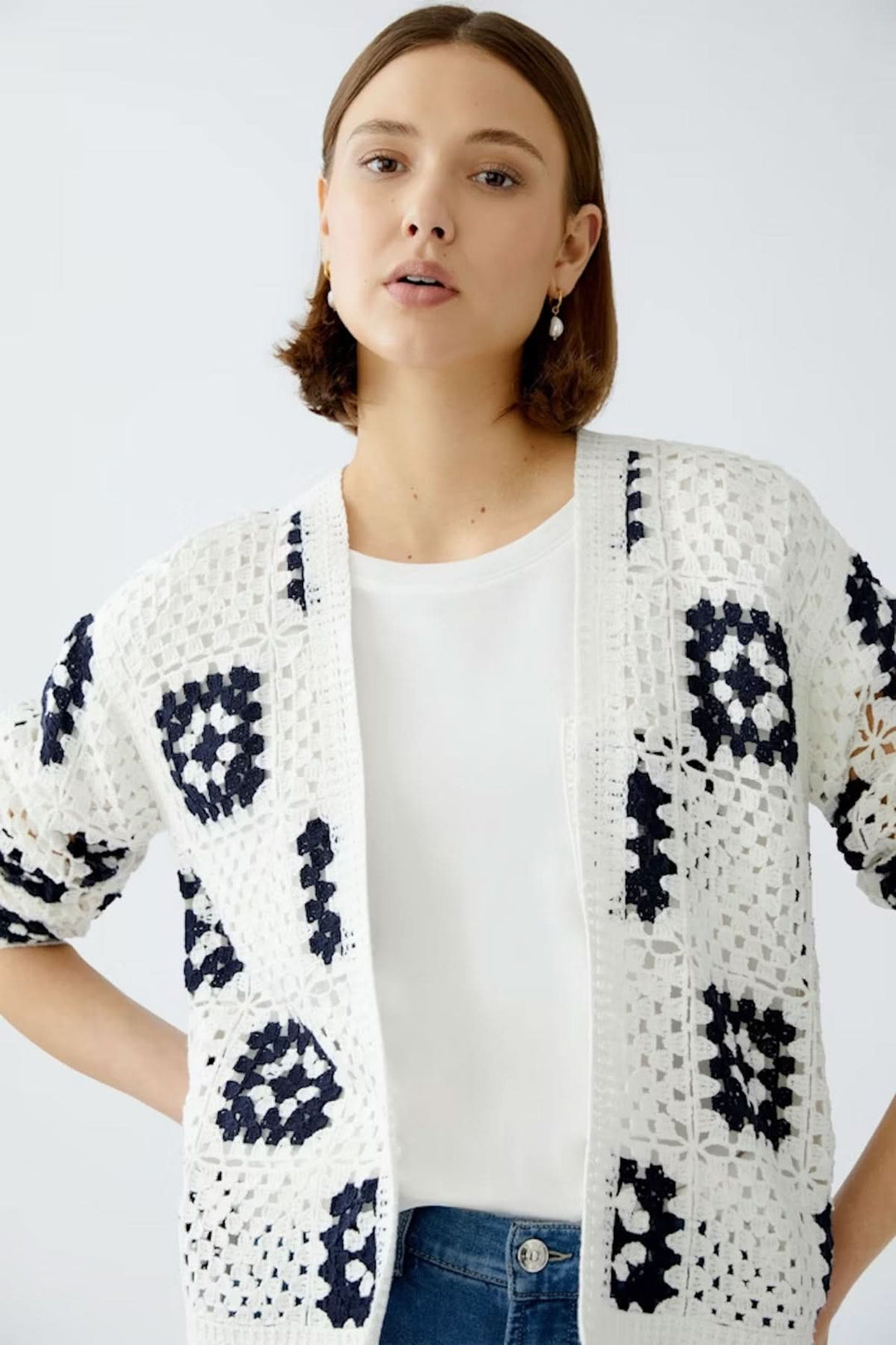 Cardigan en crochet blanc à motifs géométriques marines, porté sur t-shirt blanc et jeans bleus.