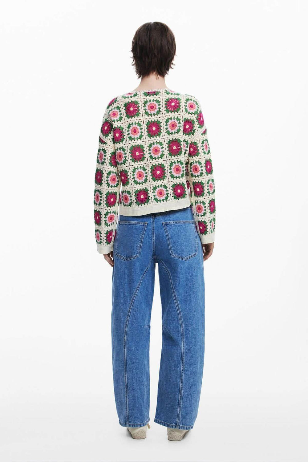 Cardigan en crochet fait main avec motifs floraux colorés, porté de dos avec jeans décontractés.