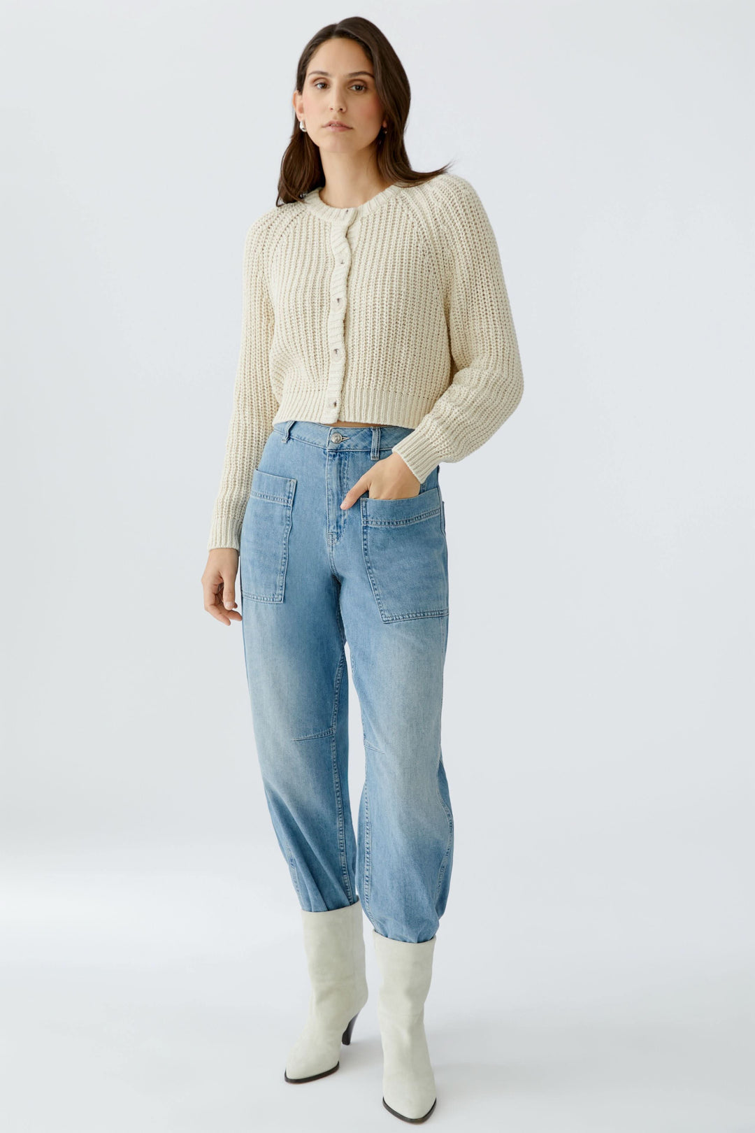 Modèle portant un cardigan en maille boutonné blanc avec un jean bleu.