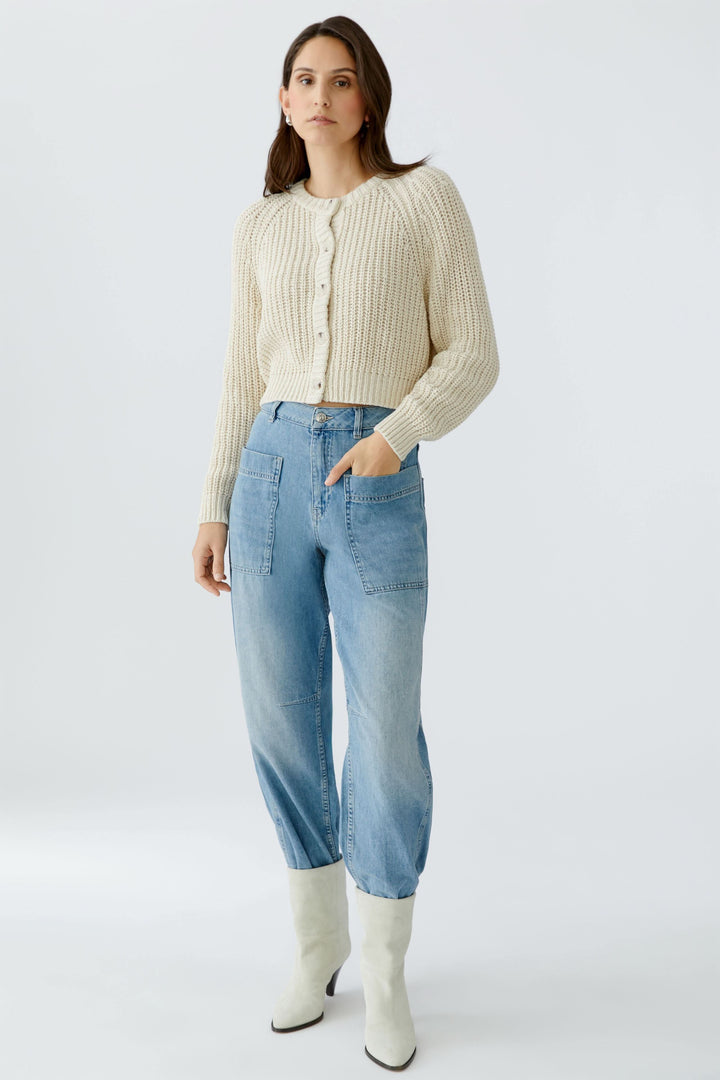 Modèle portant un cardigan en maille boutonné blanc avec un jean bleu.