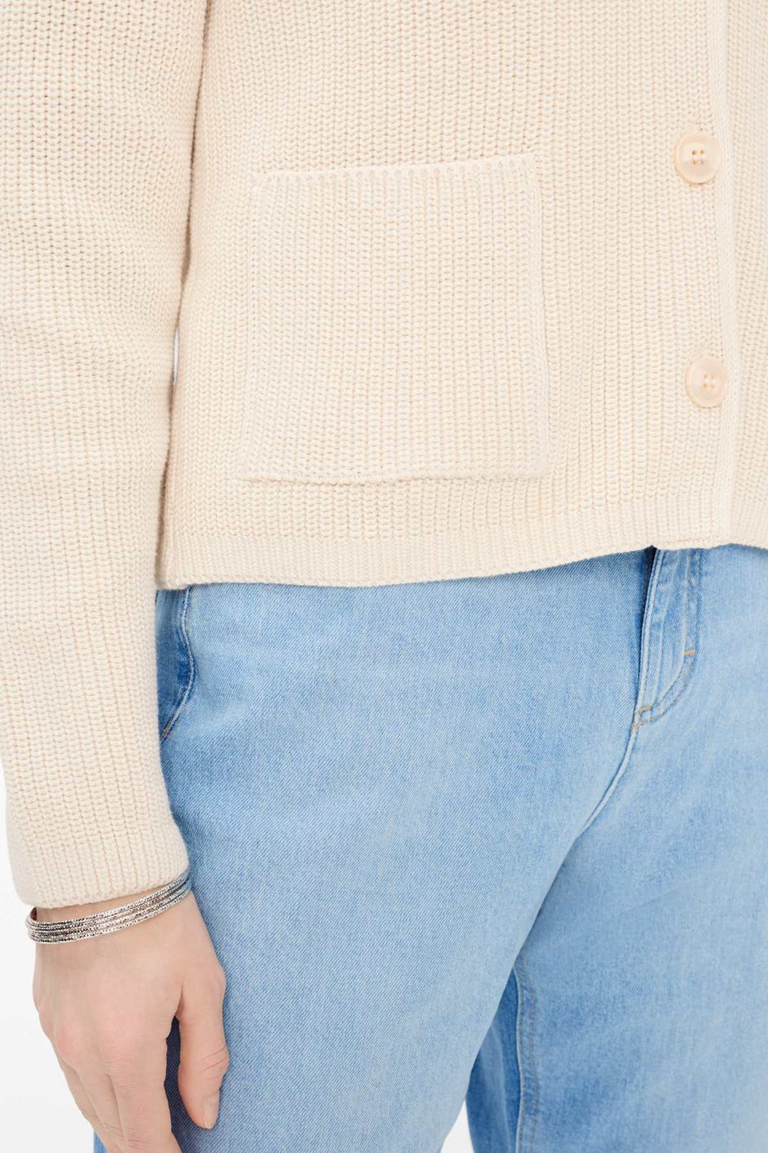 Cardigan en maille côtelée AMI, beige, avec poche avant et boutons, porté avec un jean bleu.