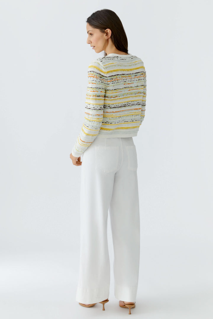 Cardigan en maille à rayures boutonné porté avec un pantalon blanc, offrant une allure élégante et structurée.
