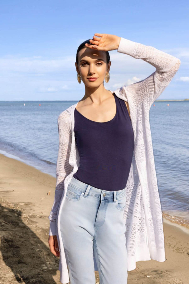 Femme portant un cardigan long en maille ajourée sur la plage, tenue décontractée pour superpositions élégantes en bord de mer.
