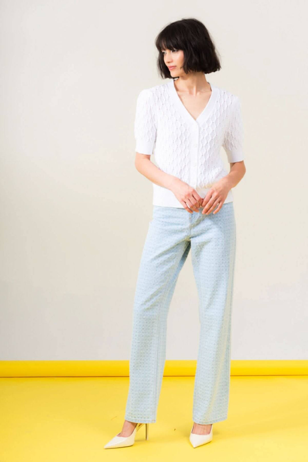 Cardigan tressé à encolure en V, manches 1/2, porté avec un pantalon léger, offrant élégance et confort.