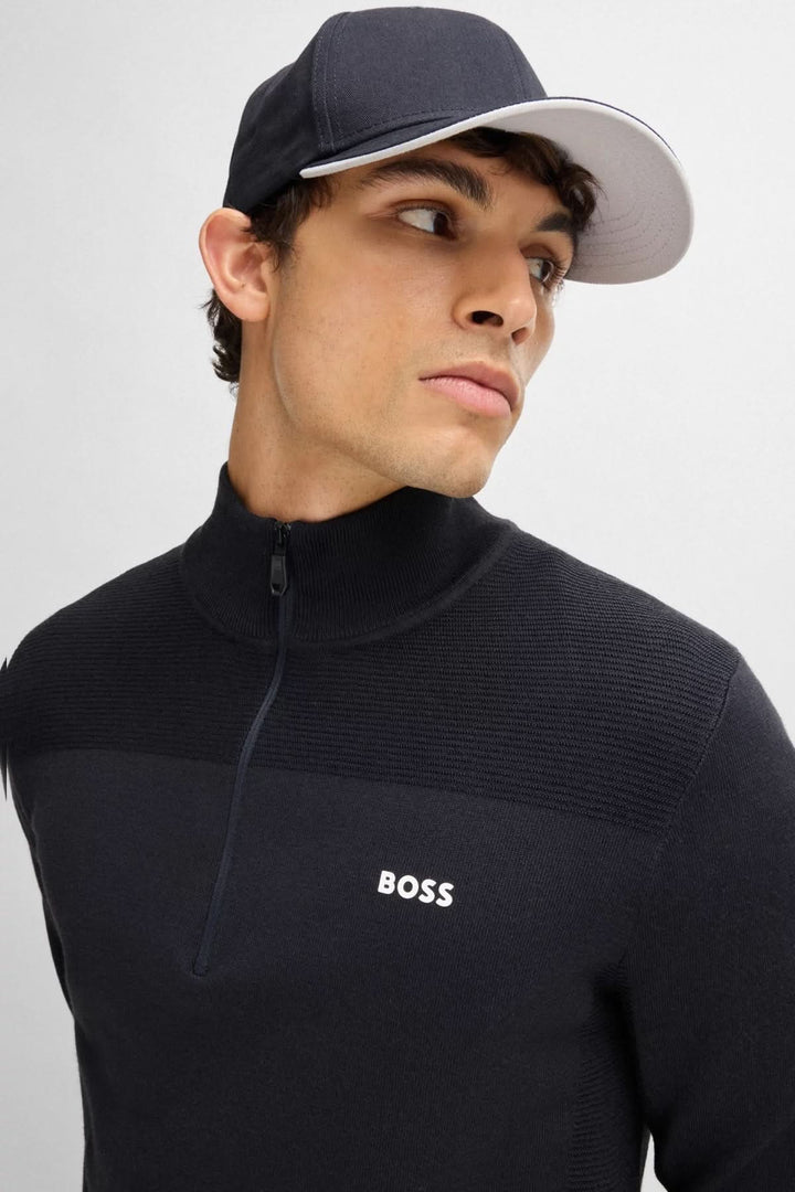 Homme portant une casquette BOSS avec visière et un pull noir à col zippé, affichant un look sportif.