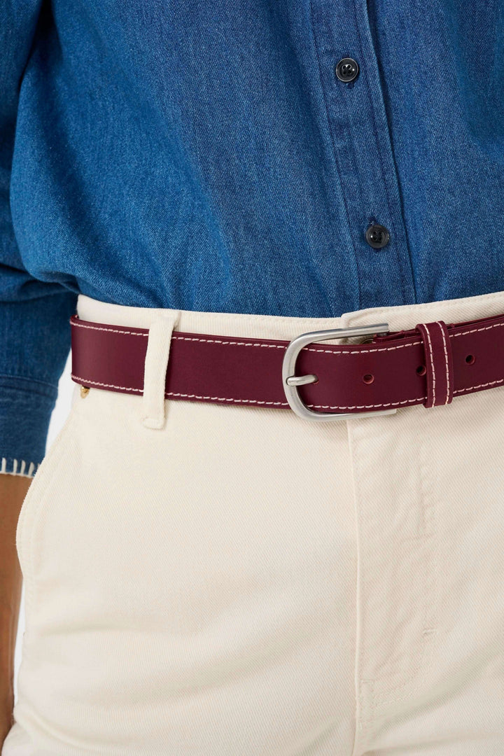 Ceinture en cuir bordeaux avec boucle classique, portée sur pantalon beige, ajoutant une touche élégante à la tenue.