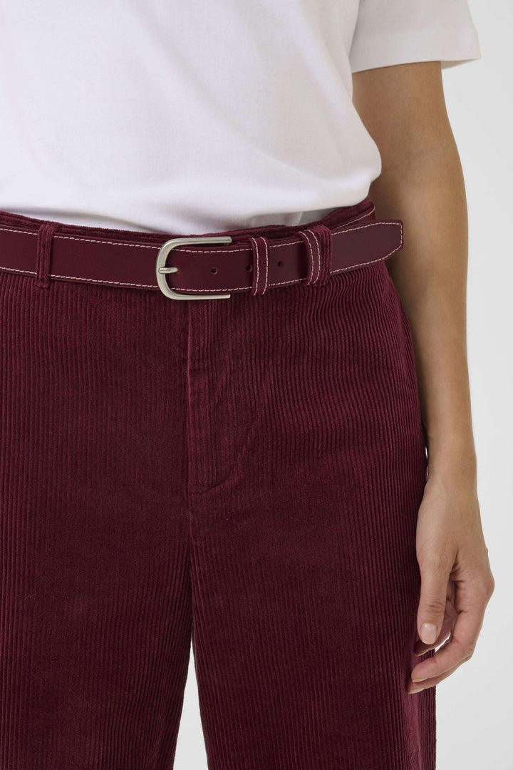 Ceinture Seyra en cuir bordeaux avec boucle métallique, portée avec un pantalon en velours côtelé. Accessoire chic.