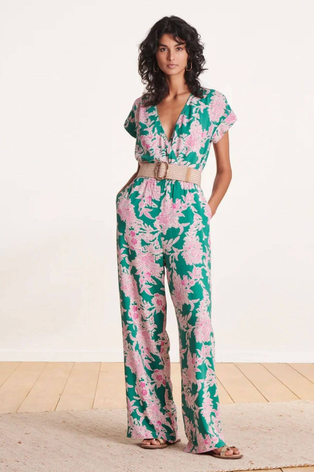 Femme en combinaison florale verte et rose, portant une ceinture large élastique beige avec boucle en laiton.