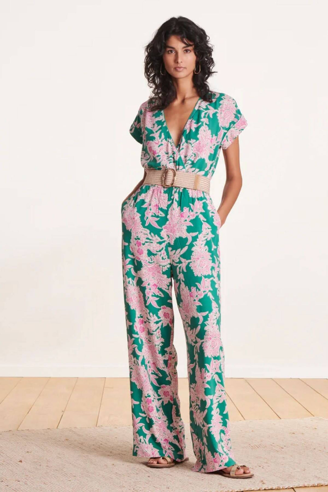 Femme en combinaison florale verte et rose, portant une ceinture large élastique beige avec boucle en laiton.