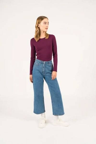 Femme portant un chandail à manches longues pourpre et un jean large dans un style décontracté.