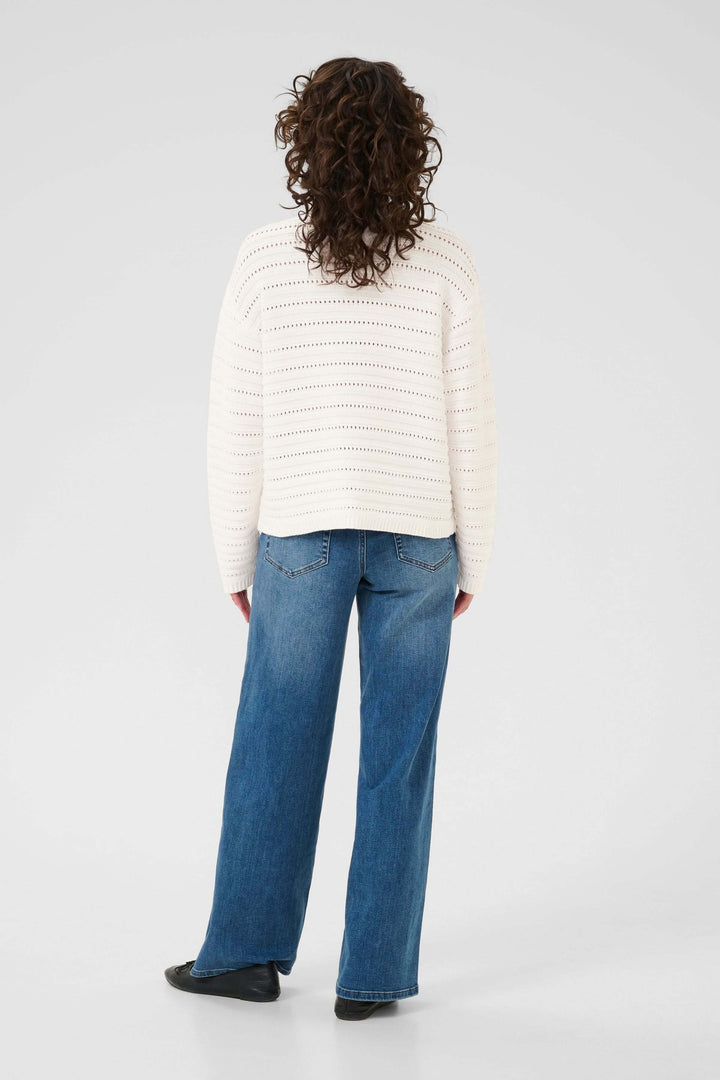 Femme portant un Chandail Dolly tricot ajouré blanc, coupe droite et col montant, de dos, avec un jean bleu et des chaussures noires.