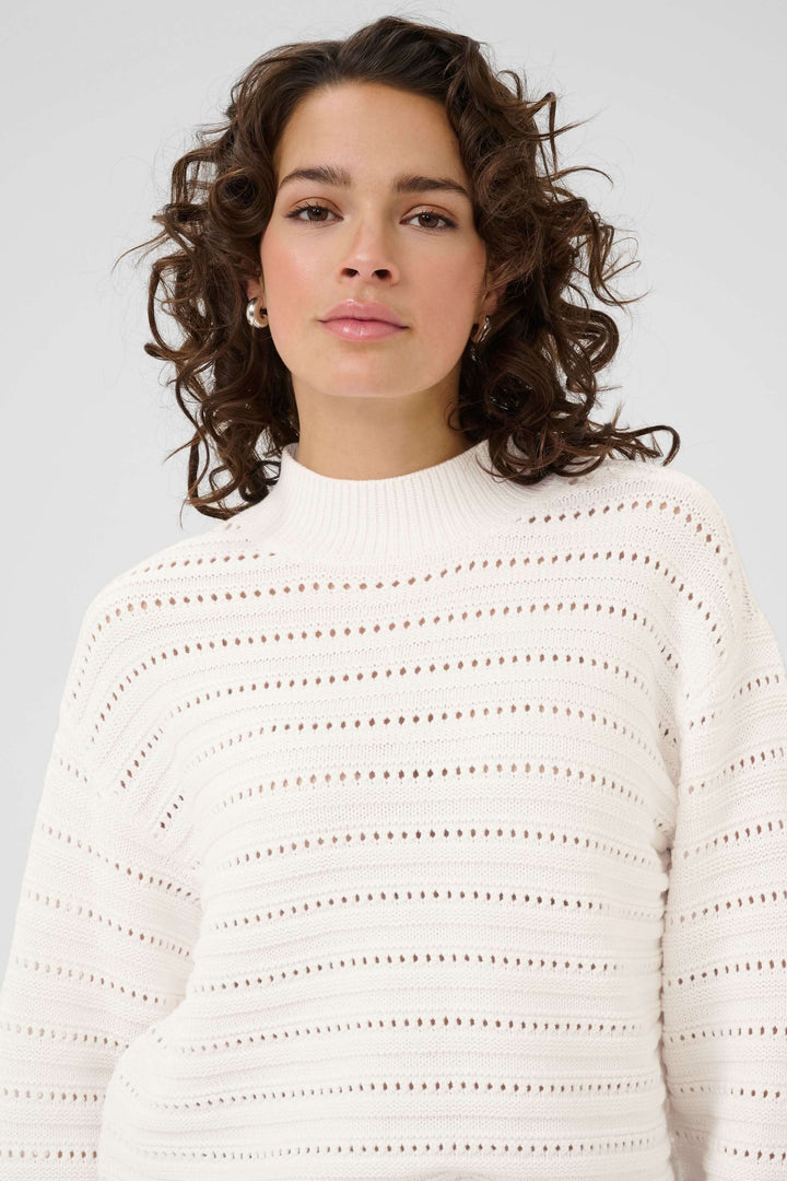 Chandail Dolly en tricot ajouré blanc, avec motif subtil et col montant, porté par un modèle pour un look moderne et chic.
