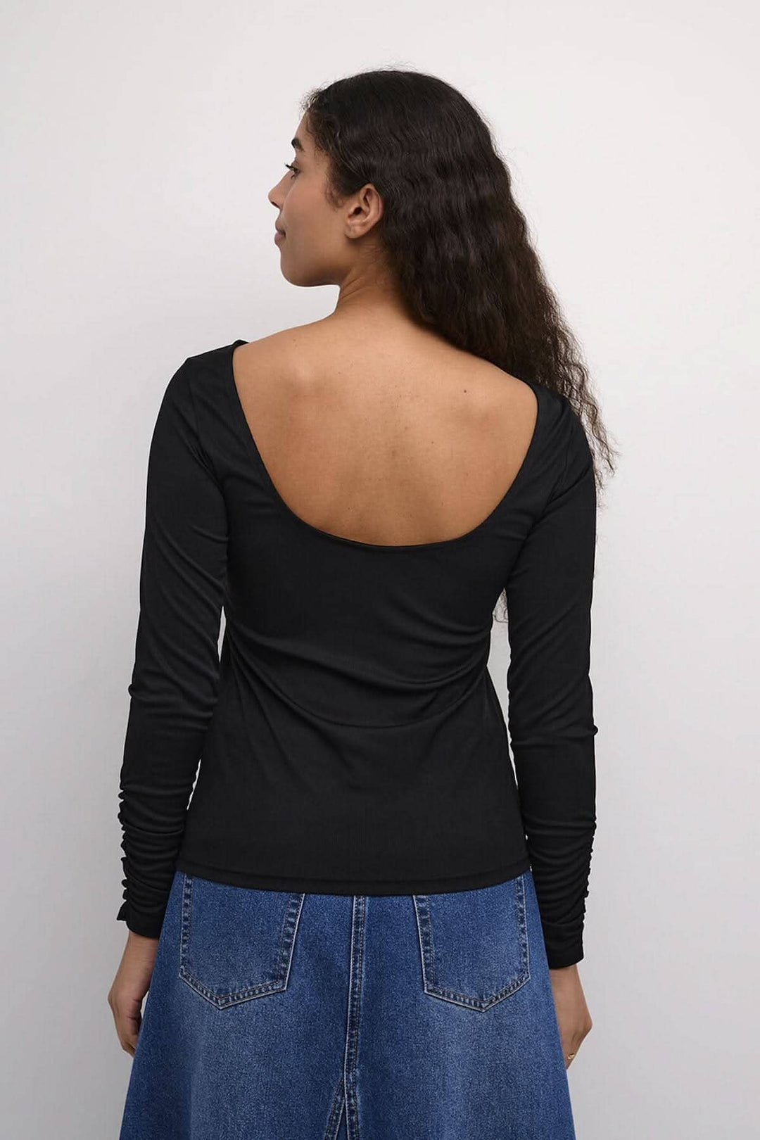 Chandail Kaffe noir à dos dégagé porté par une femme, vue de dos avec manches longues et élastiques aux poignets.