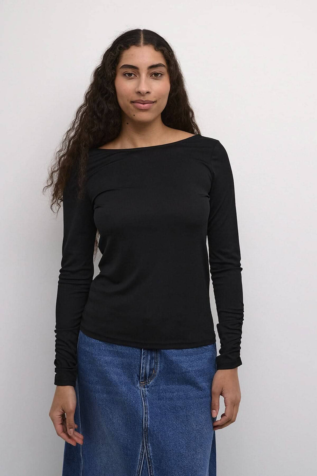 Chandail noir Kaffe à manches longues, élégant avec dos dégagé, porté avec jupe en denim.