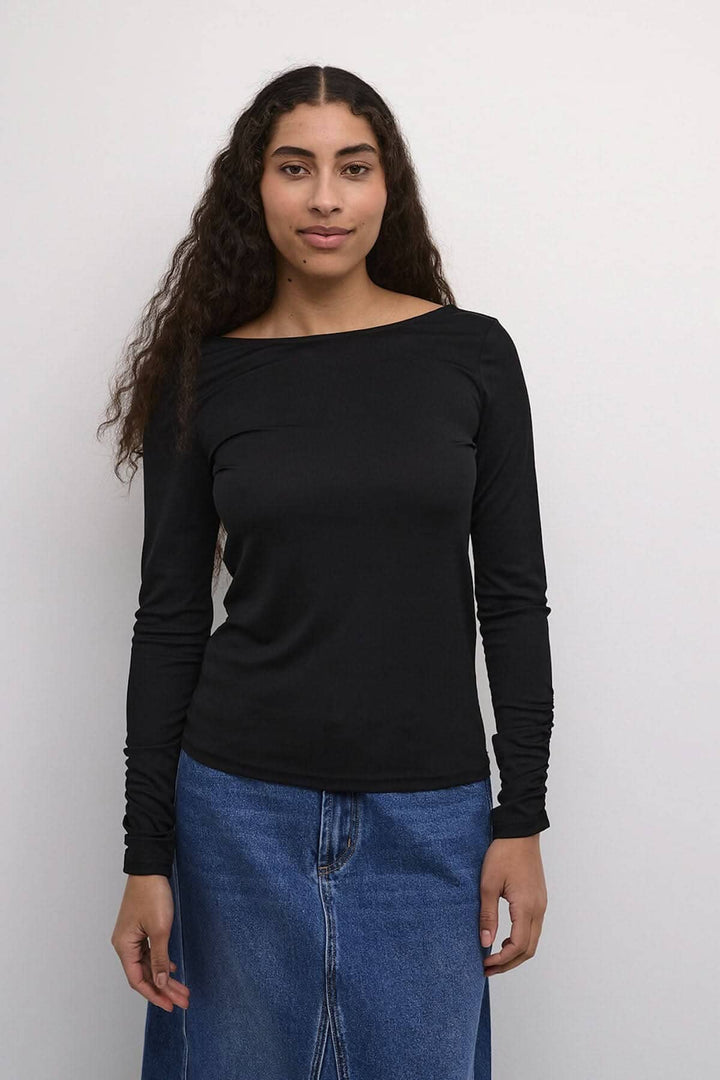 Chandail noir Kaffe à manches longues, élégant avec dos dégagé, porté avec jupe en denim.