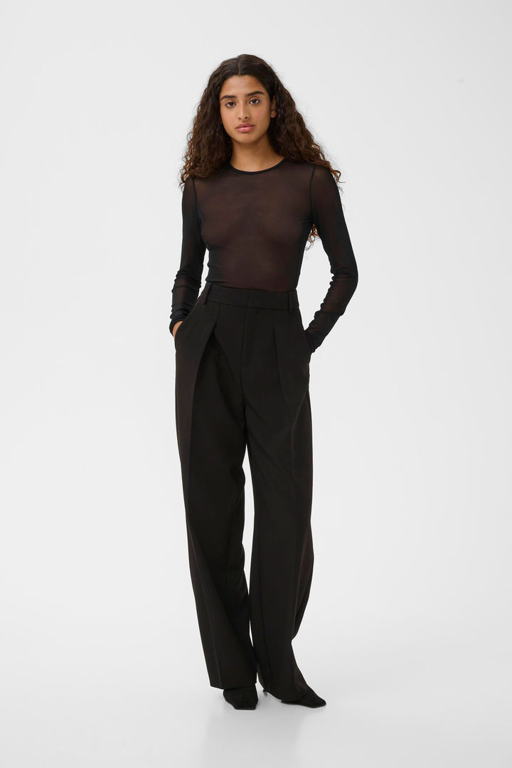 Femme portant le Chandail Kaia en tulle transparent à manches longues avec un pantalon élégant noir.