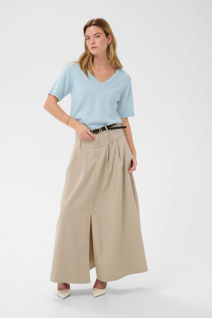 Chandail Liliana en tricot à col en V festonné porté avec une jupe longue beige, ajoutant une touche élégante et féminine.