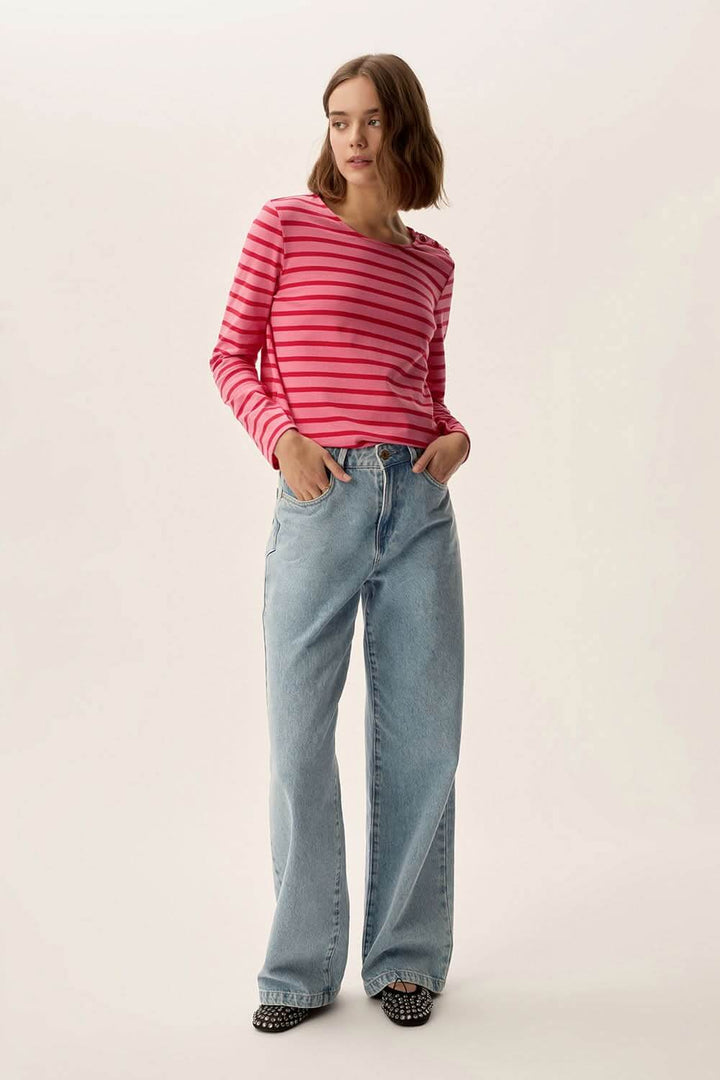 Modèle portant un chandail marinière rayé rose avec jeans décontractés en denim, look tendance et authentique.