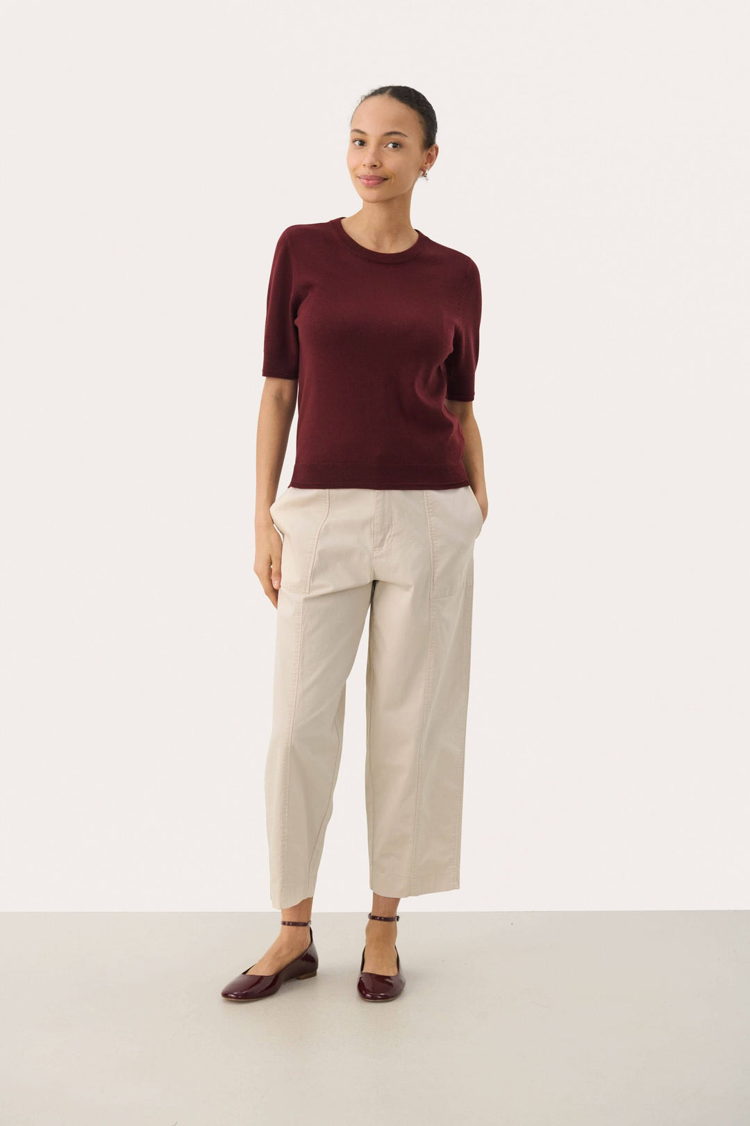 Chandail Natanya en tricot bordeaux à manches courtes, porté avec un pantalon clair pour un look élégant.