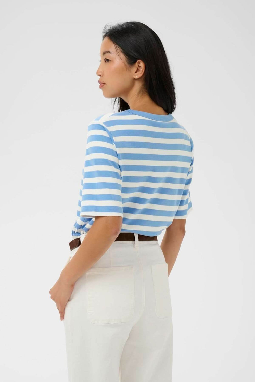 Chandail Ratana ligné à rayures bleues et blanches, porté par une femme de dos avec pantalon blanc.